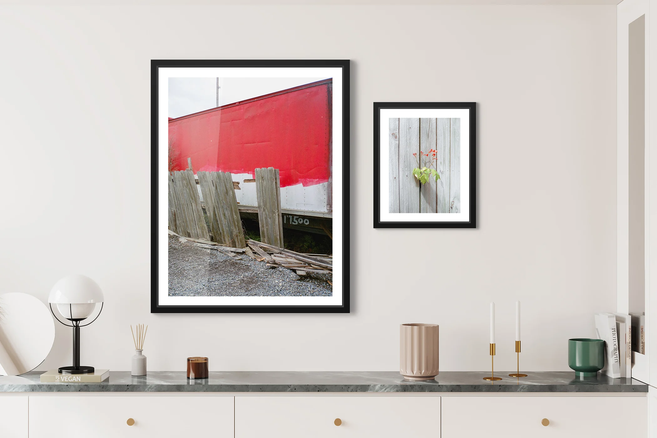 On the left a broken wood fence in front of a train which is partially painted red and on the right a plant with small red flowers peeking through a dense wooden fence. On the left a broken wood fence in front of a train which is partially painted red and on the right a plant with small red flowers peeking through a dense wooden fence.