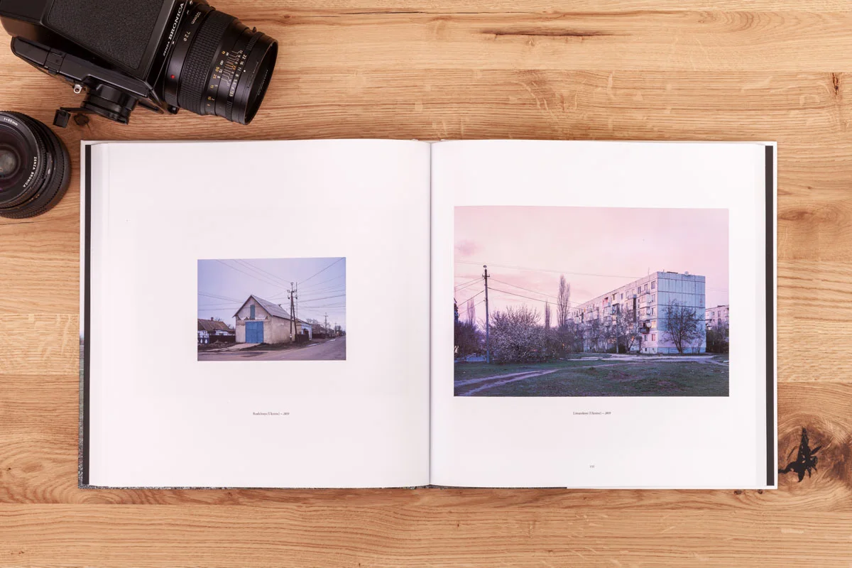 Offenes Fotobuch mit zwei Bildern auf einer Holzoberfläche, daneben eine Kamera und ein Objektiv. Offenes Fotobuch mit zwei Bildern auf einer Holzoberfläche, daneben eine Kamera und ein Objektiv.
