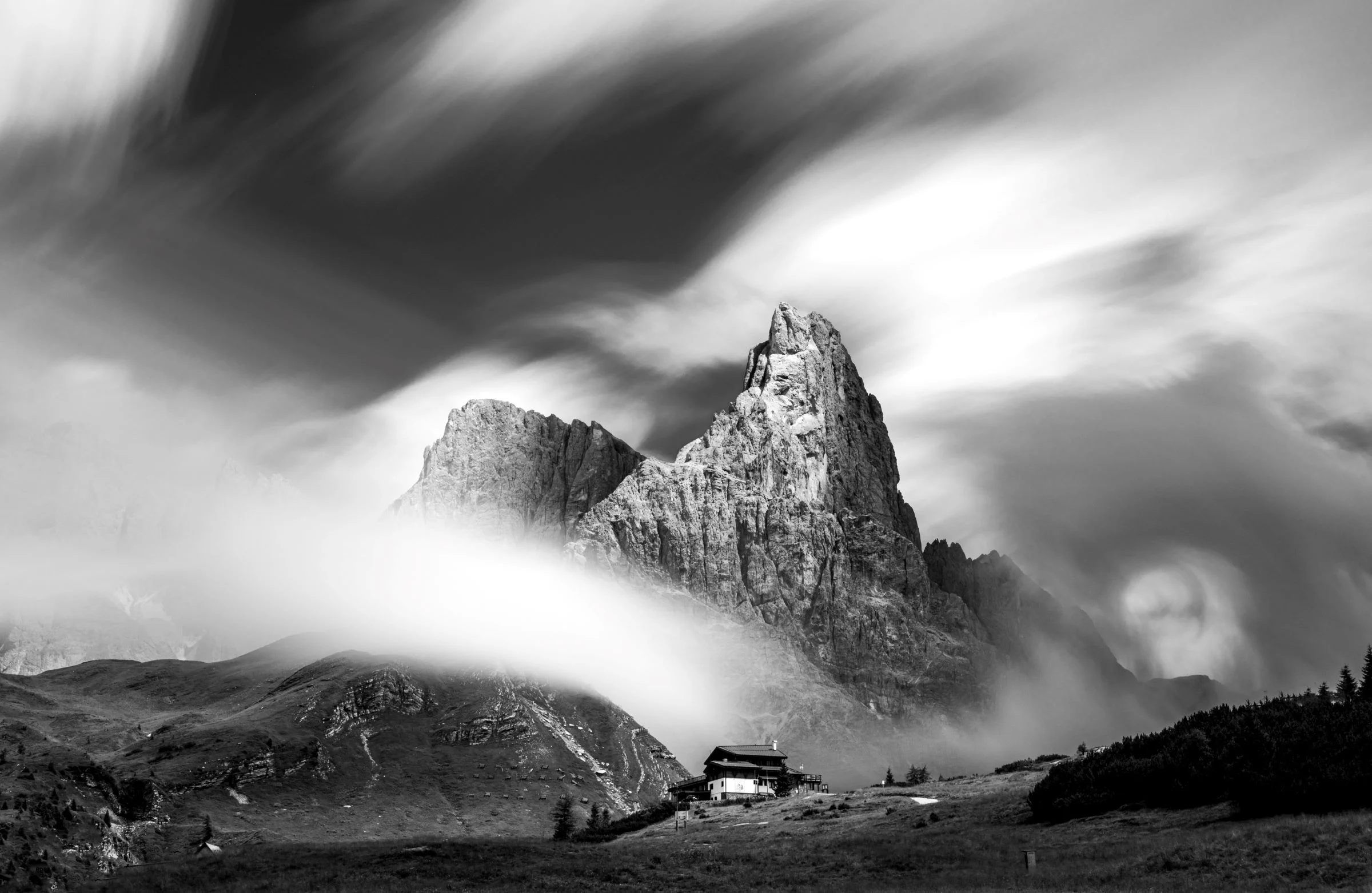 Black and white image of a mountain with clouds and a building in the foreground. Black and white image of a mountain with clouds and a building in the foreground.