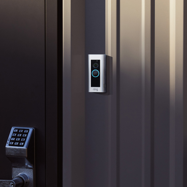 Ring Video Doorbell with a blue-lit button mounted beside a keypad lock on a metal door.