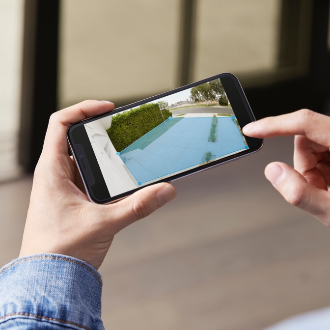 A person uses the Ring App to adjust motion detection zones over a live camera view of a driveway and front yard.