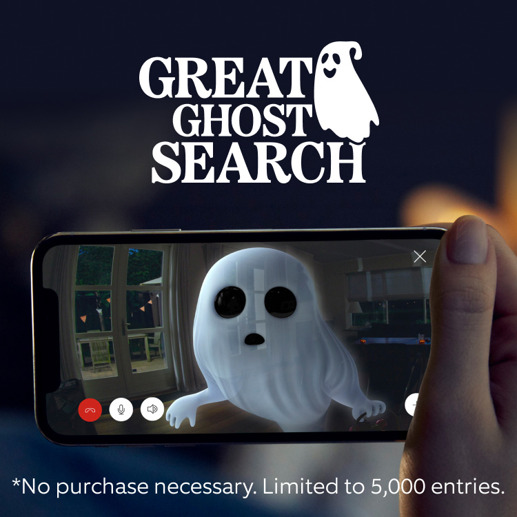 Hand holding a smartphone displaying Ring camera footage of cartoon ghost in a home being scared off by camera.