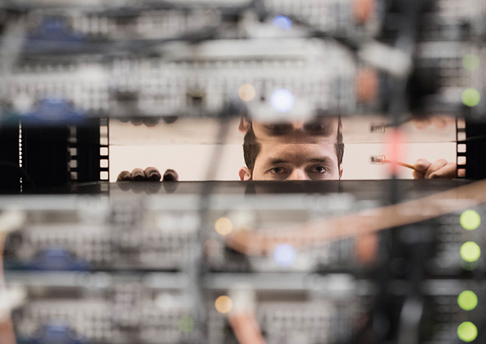 Man peering between a stack of servers