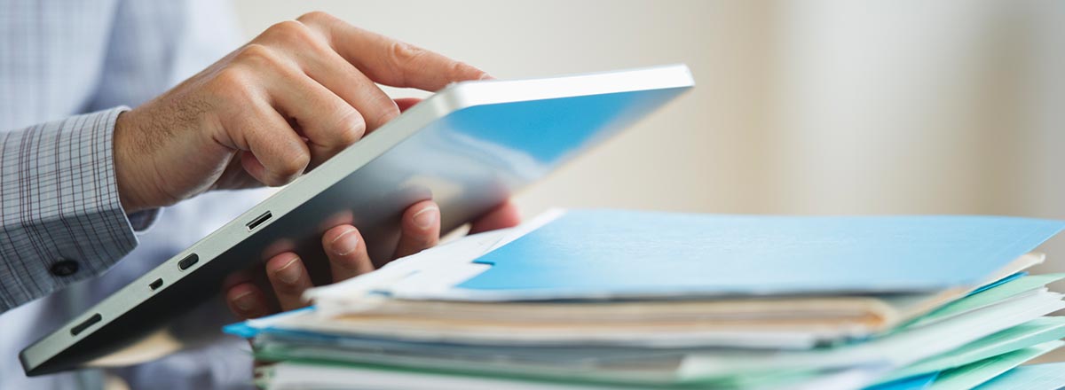 Business person with a tablet and a stack of folders full of paper documents