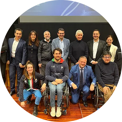 Gruppo di persone sorridenti che guardano verso la telecamera, alcune in piedi e altre in sedia a rotelle.