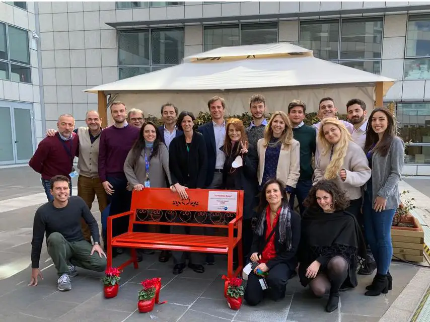 Un gruppo di persone accanto alla panchina rossa di una sede P&G con le fioriere a forma di scarpa rossa