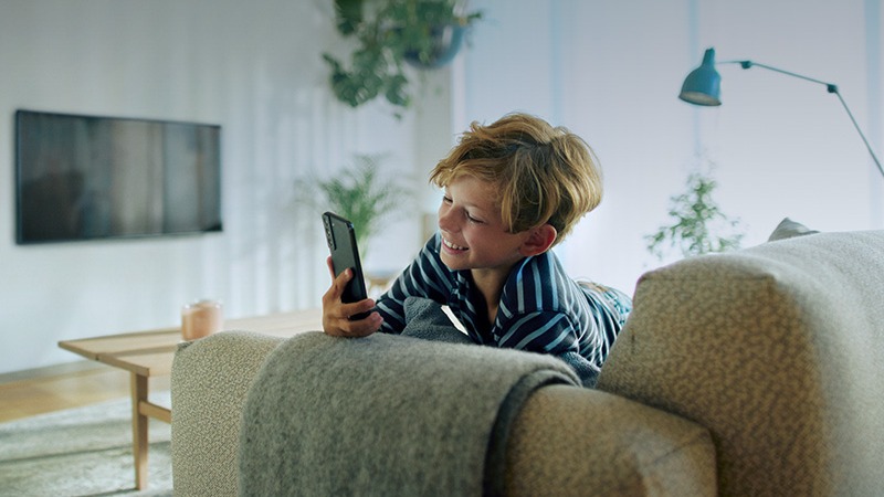 Pojke sitter i soffan och tittar på sin mobil