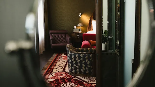 Et rundt speil reflekterer et koselig rom med sofa, mønstret teppe og stemningsfull belysning, som tyder på et intimt innemiljø.