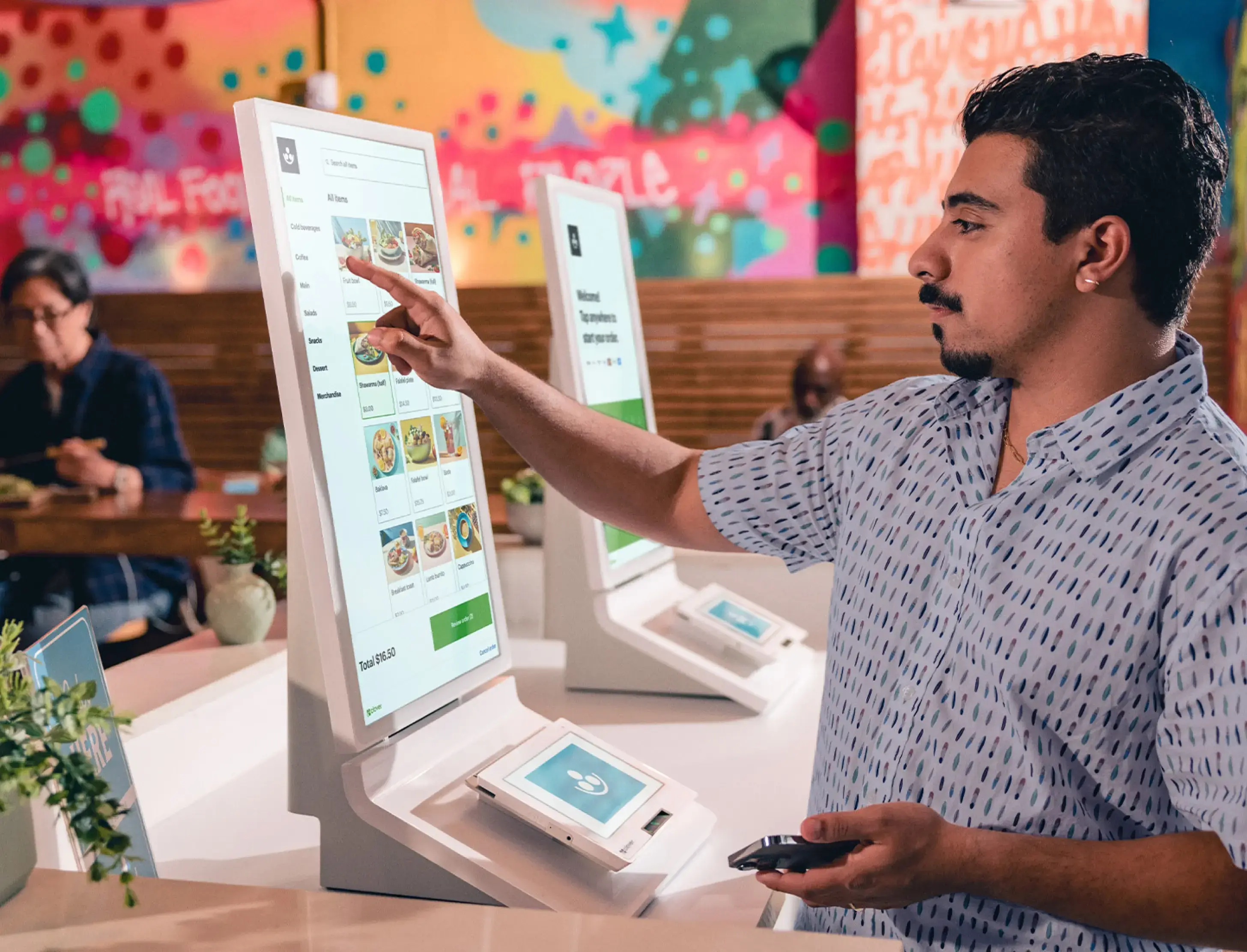 Customer standing in front of one of the table mounted Clover Kiosks browsing menu items.