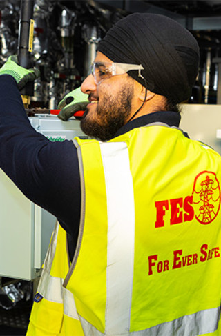 Young smiling man in high-vis waistcoat operating a machine in an industrial building