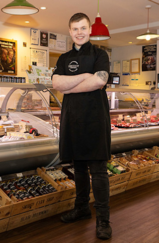 Young smiling man in black uniform, standing next to food counter in a shop