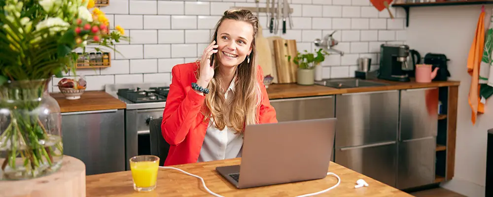 Bellende vrouw zit met haar laptop voor zich aan de keukentafel.