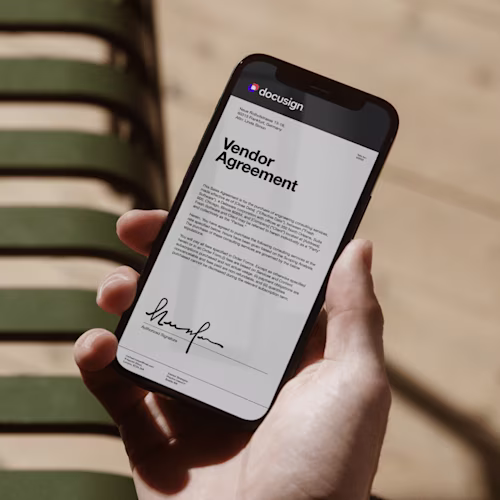 Person holding phone showing Docusign logo while working on a laptop