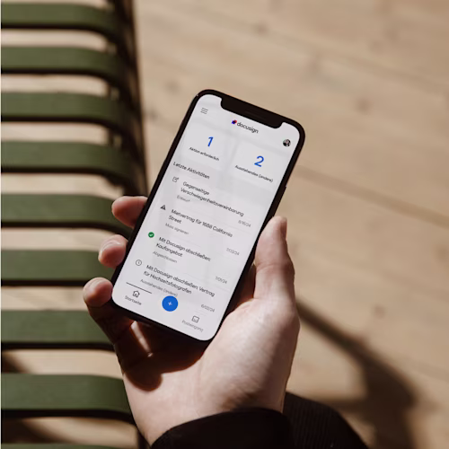 A hand holding a phone showing a dashboard in Docusign with required actions and recent activity