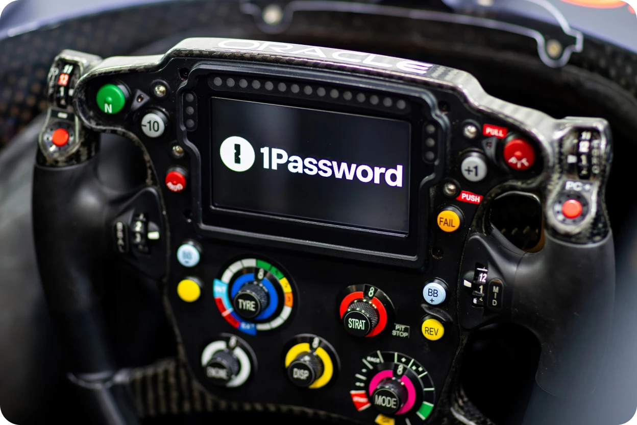 Close-up of an Oracle Red Bull Racing F1 car's steering wheel, featuring a digital display with the 1Password logo, showcasing the partnership between 1Password and Oracle Red Bull Racing.
