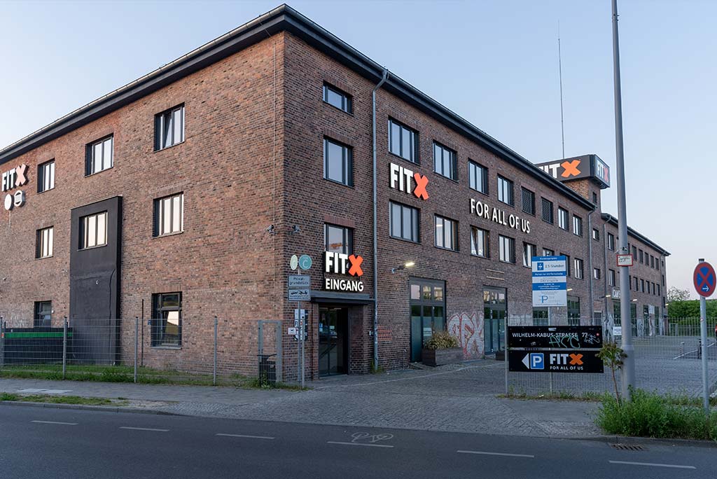 Außenansicht des FitX Fitnessstudios Berlin-Südkreuz. Ein großes FitX-Logo mit orangefarbenem X ist zu sehen. Das Gebäude befindet sich in einem urbanen Umfeld.