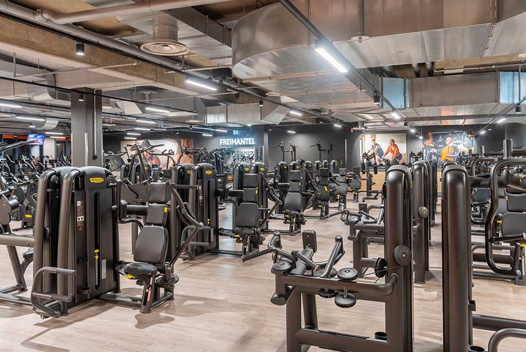 Gerätebereich im FitX Fitnessstudio Berlin-Schöneberg mit verschiedenen Kraftgeräten. Der Raum ist im industriellen Design gestaltet, mit offenen Deckenstrukturen und hellen Böden.