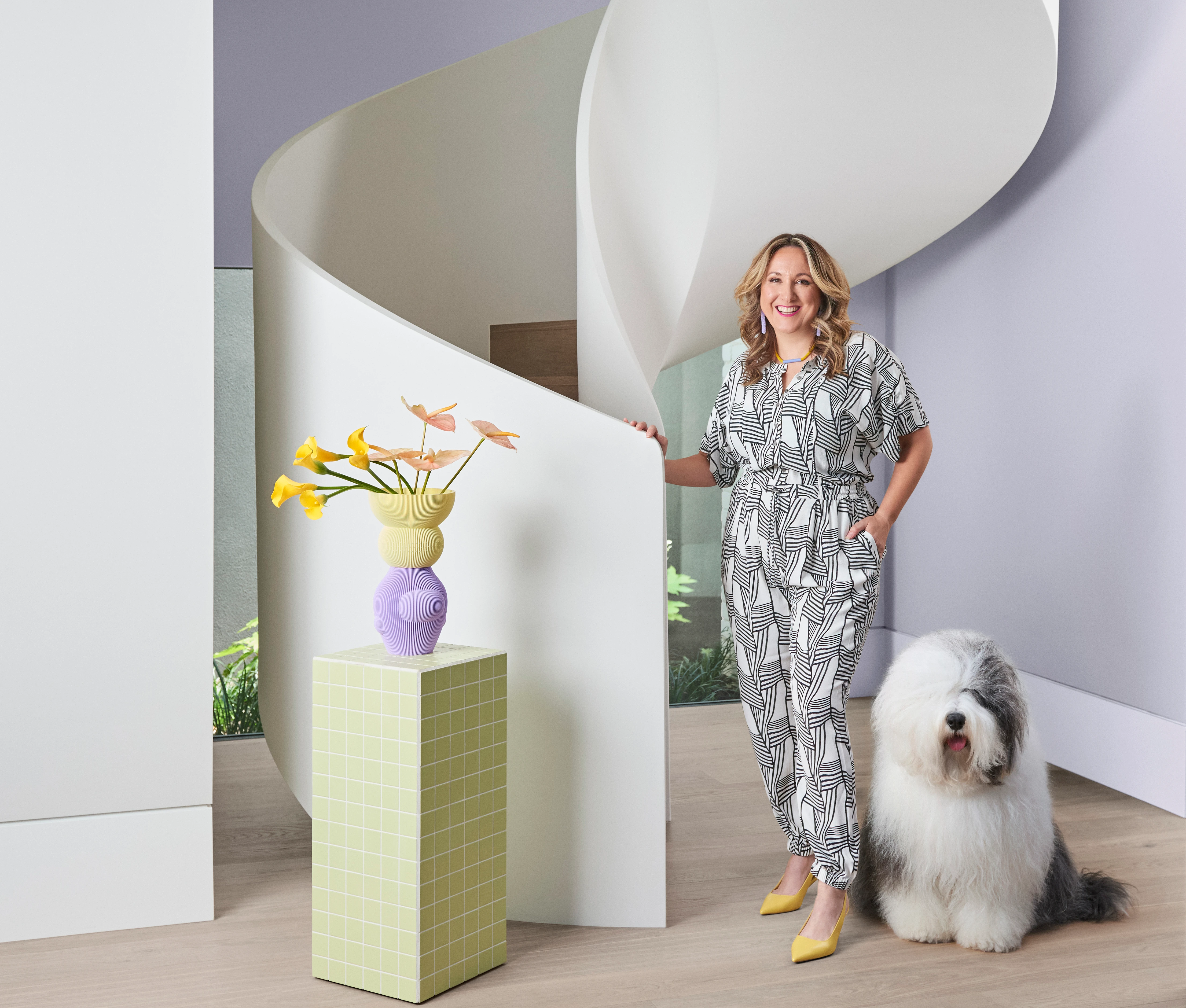Bree Leech leaning against twisting white stair case with Dulux dog sitting next to her.