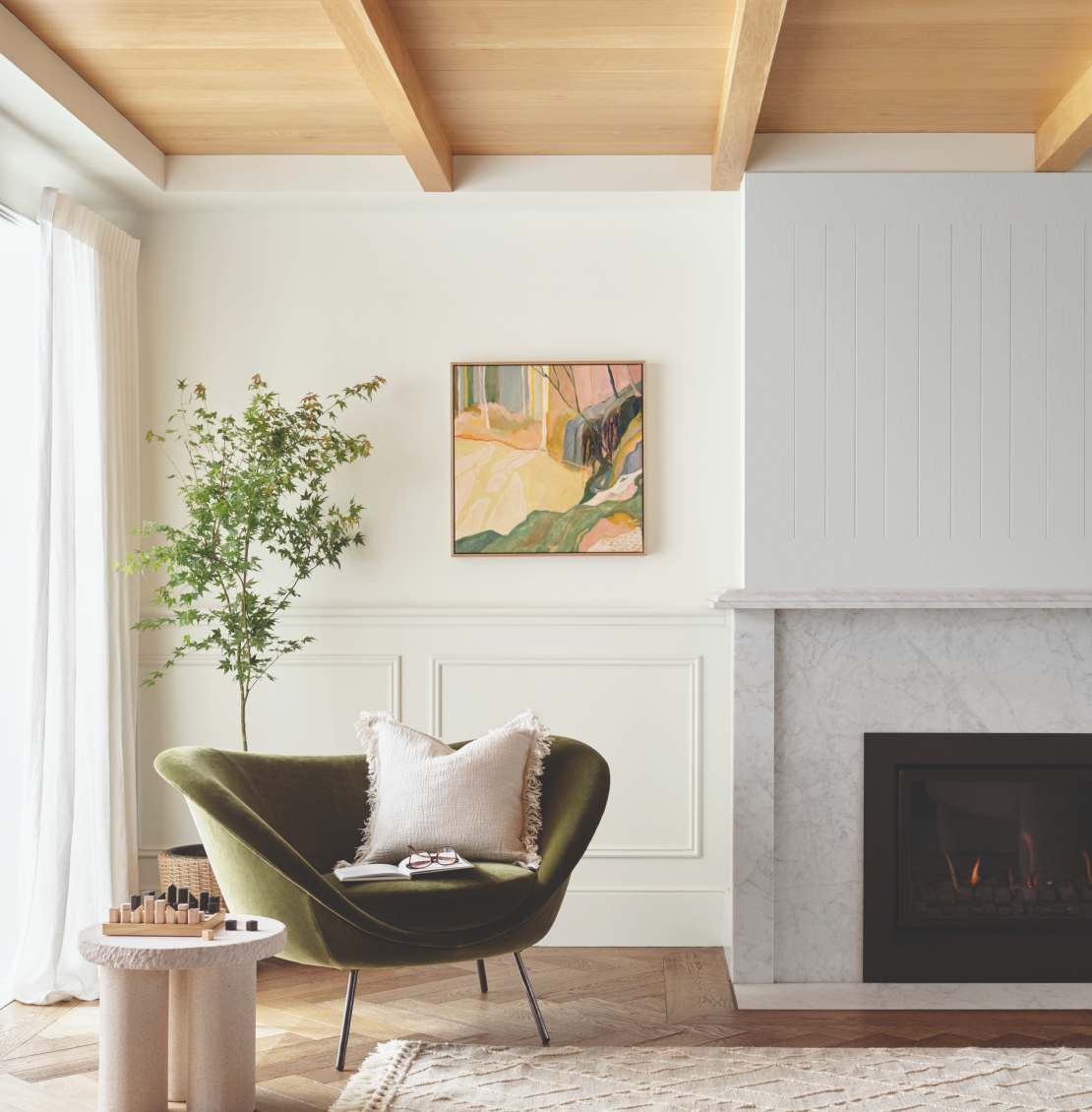 White living room with exposed timber beams ceiling, marble mantle, and green velvet armchair.