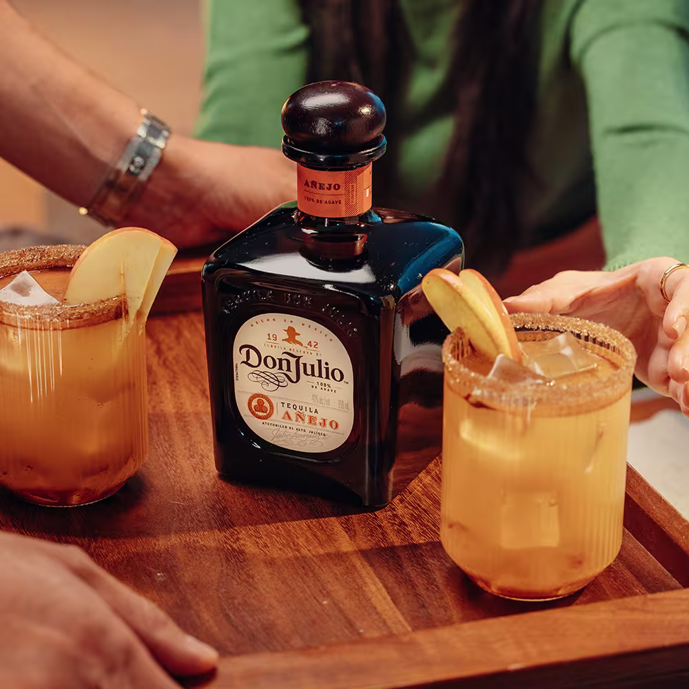 Two Apple Cider Margaritas on a board alongside a bottle of Don Julio Añejo