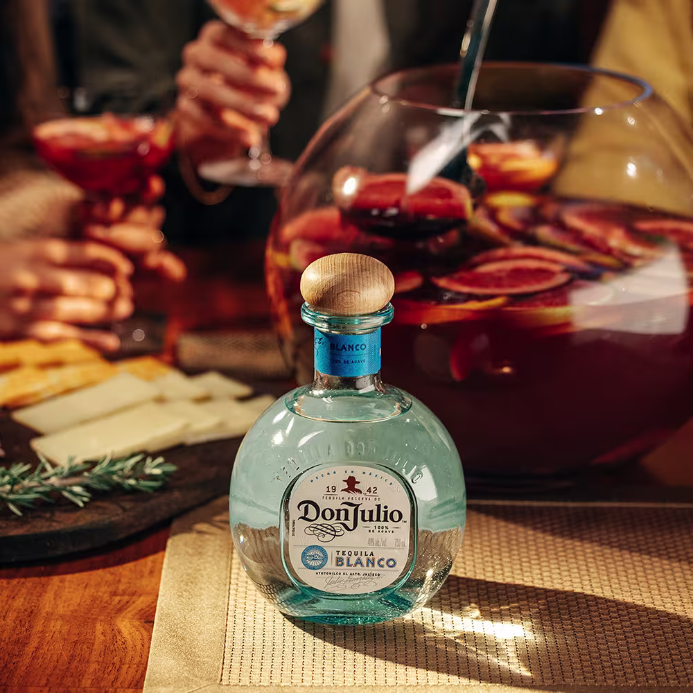 A bottle of Don Julio Blanco on a table with a bowl of Tequila Sangria behind it
