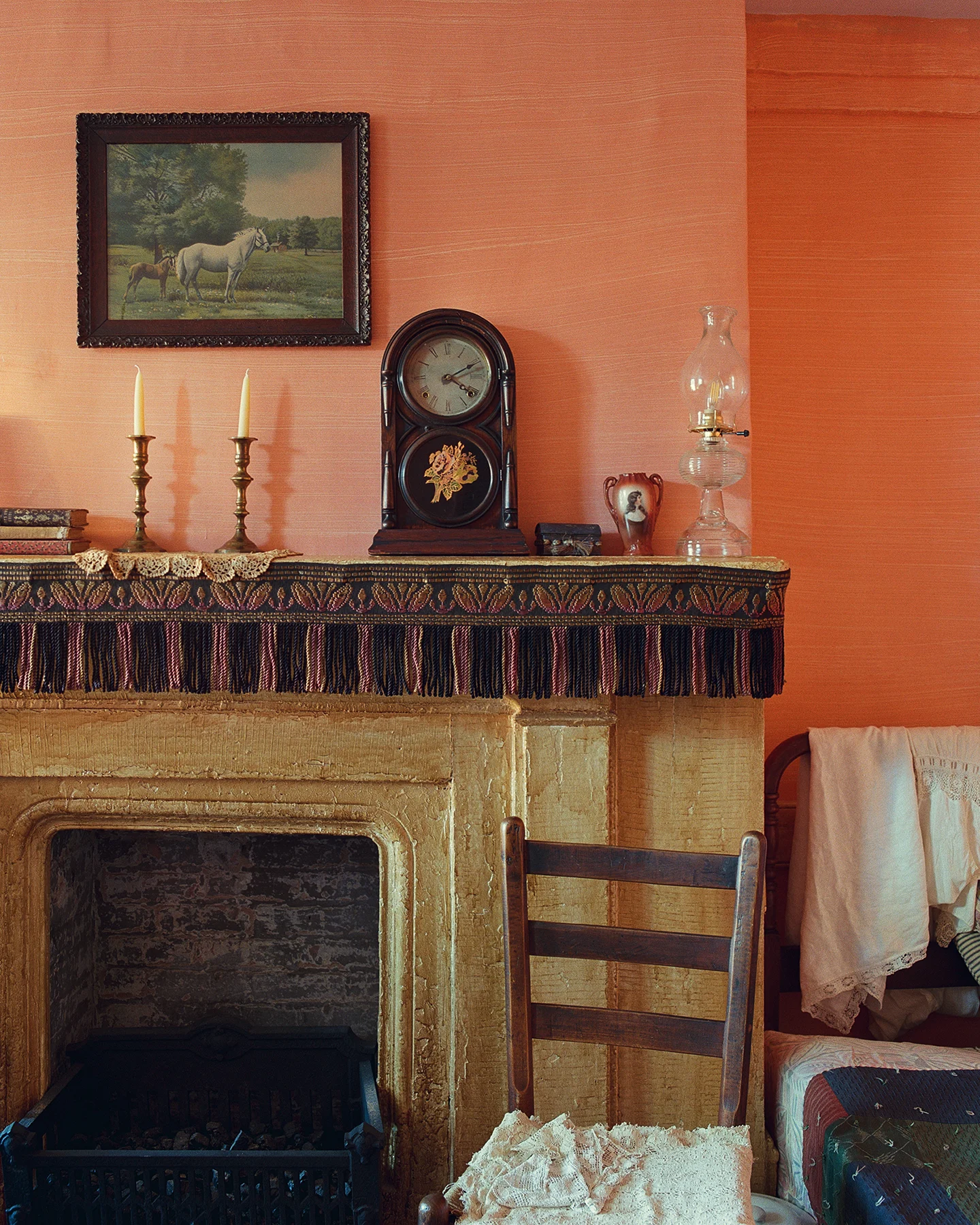 A fireplace mantle is adorned with objects collected from 19th century America: books, candlesticks, a wooden clock, porcelain items and a glass lantern