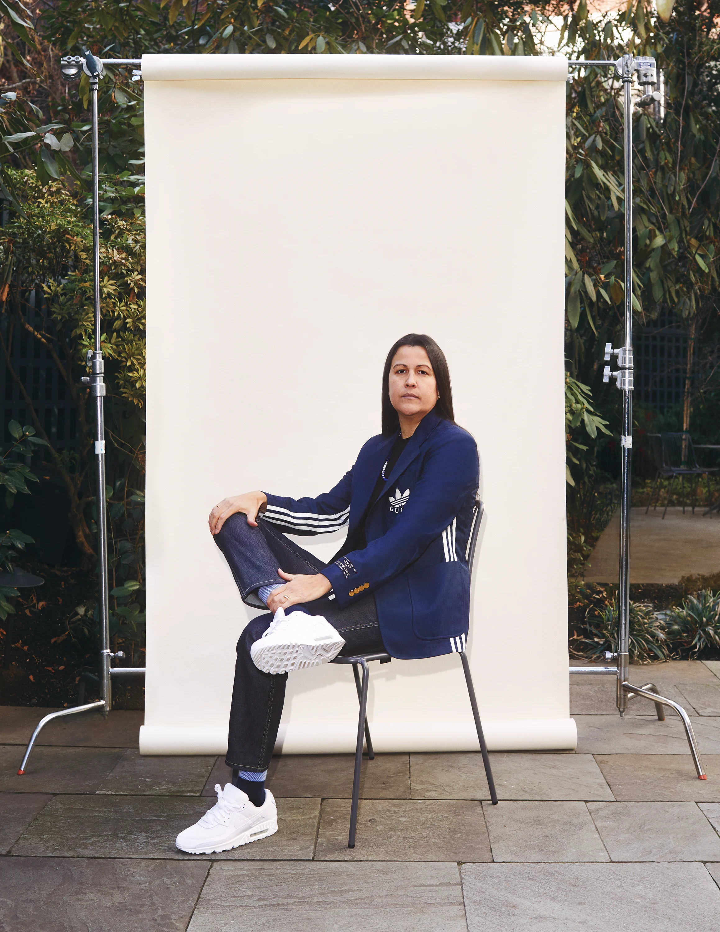A vertical image of an Indigenous person who is sitting on a chair in front of a backdrop.