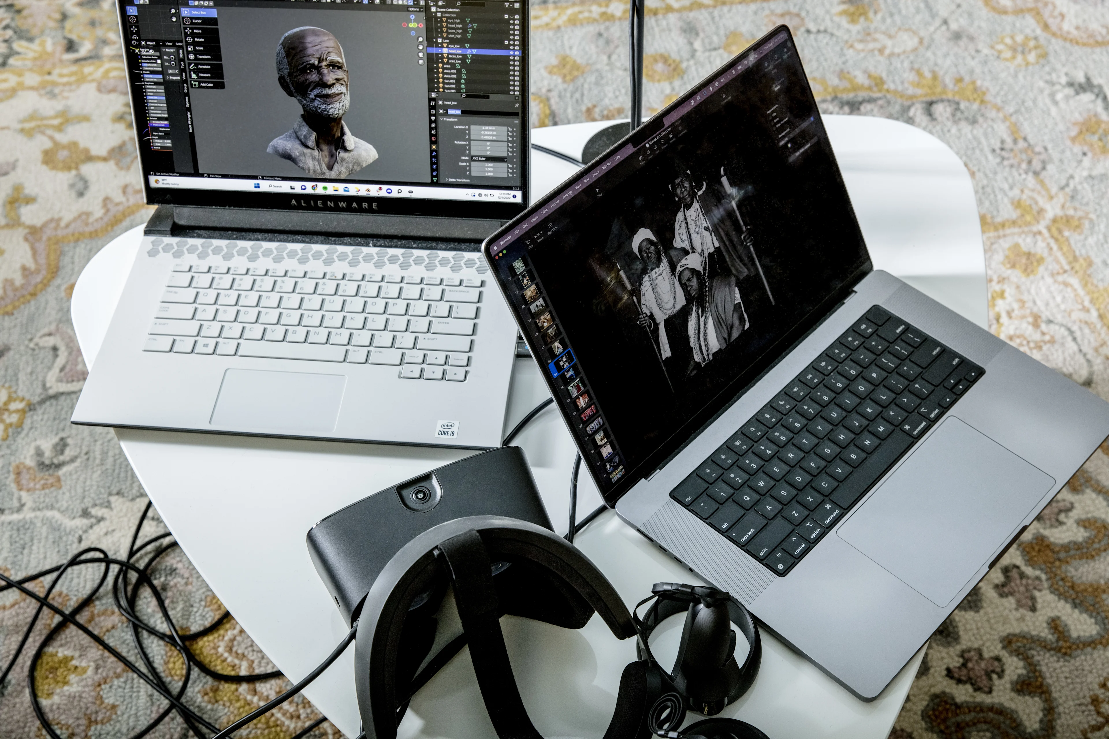 Two open laptops are sitting on a coffee table. The screens are visible and display computerized renderings of historical figures. A VR headset is also visible.