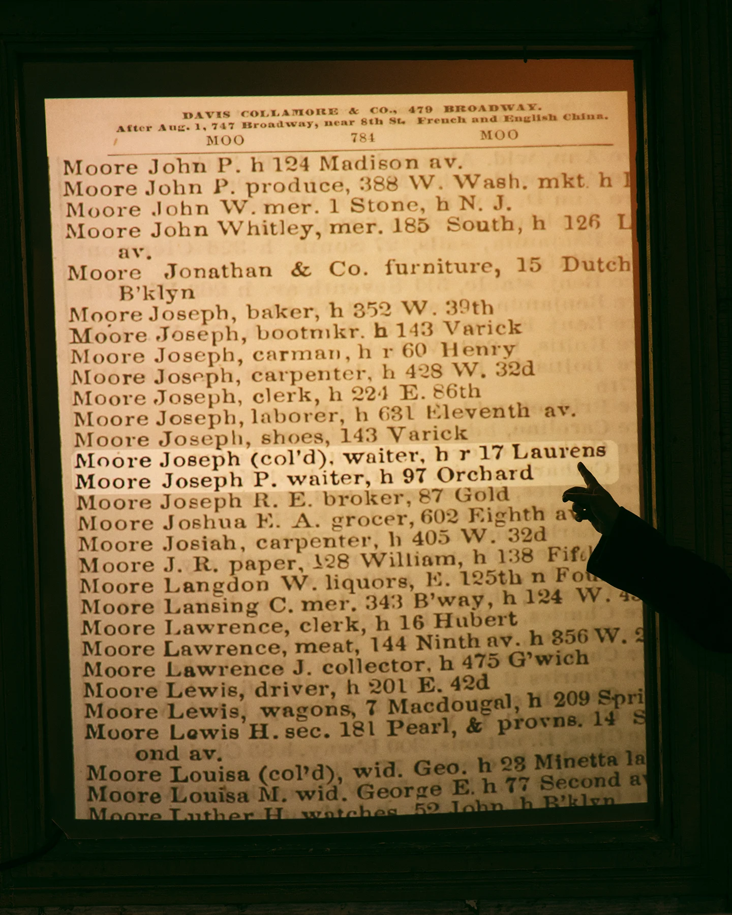 A detailed list of 19th century New York residents in alphabetical order by last name. A hand, in sillouette, points to an entry, “Joseph Moore”