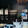 Kaffemaskiner står på en benk og serverer drikker. Hyller holder glass. I forgrunnen er det boller med frokostvarer. Et skilt med teksten "PERSONAL STAFF" vises på en dør.