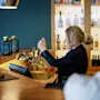 Bartender häller upp öl från en kran i ett glas, på en bar med en trädisk och flaskor i bakgrunden.