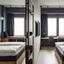 A modern hotel room features two beds separated by a partition, with a desk and chair in front of large windows, and dark curtains providing a cozy ambiance.