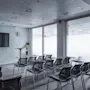 En rad svarta stolar vetter mot en stor skärm i ett konferensrum. Rummet har en grå matta, glasväggar och en krukväxt nära skärmen.