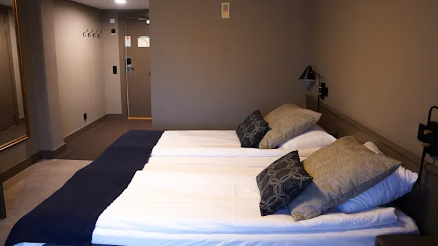 En snyggt bäddad säng med kuddar i ett prydligt hotellrum med nedtonad belysning.