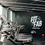 Tredemøller står på rad i et moderne treningsstudio med elegante mørke interiører. En vegg viser teksten "FIT AND FAB BY SELMA CITY SPA." En oransje treningsball ligger på gulvet.