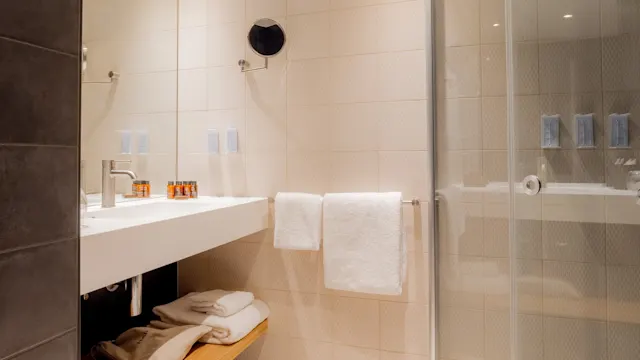 Et moderne baderom med vask, speil og dusjhjørne av glass, kontrasterende mørke og lyse fliser.