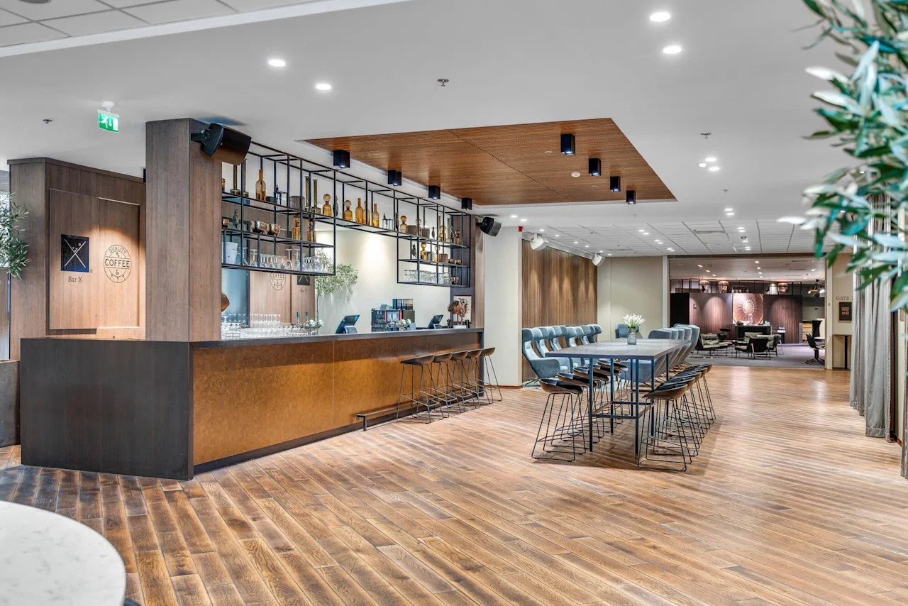 En moderne hotellobby med trægulv, en kaffebardisk, stole og borde; varmt lys skaber en indbydende atmosfære.
