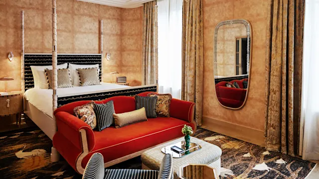 Et luksuriøst soverom med himmelseng, rød sofa, elegante gardiner, og en dekorativ speil, som viser frem rike teksturer og varme toner.