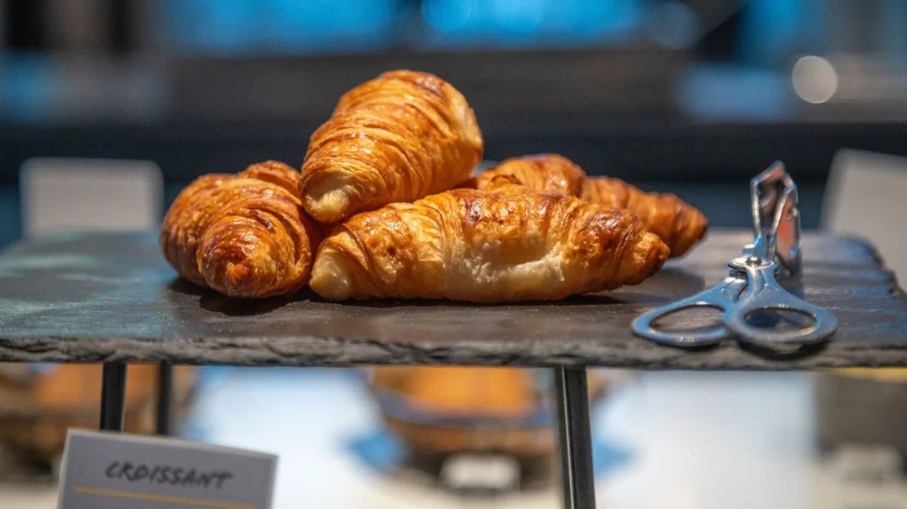 Croissanter med gyllenbrun färg ligger på ett skiffertack med silvertillbehör bredvid; oskarp bakgrund i bageri.