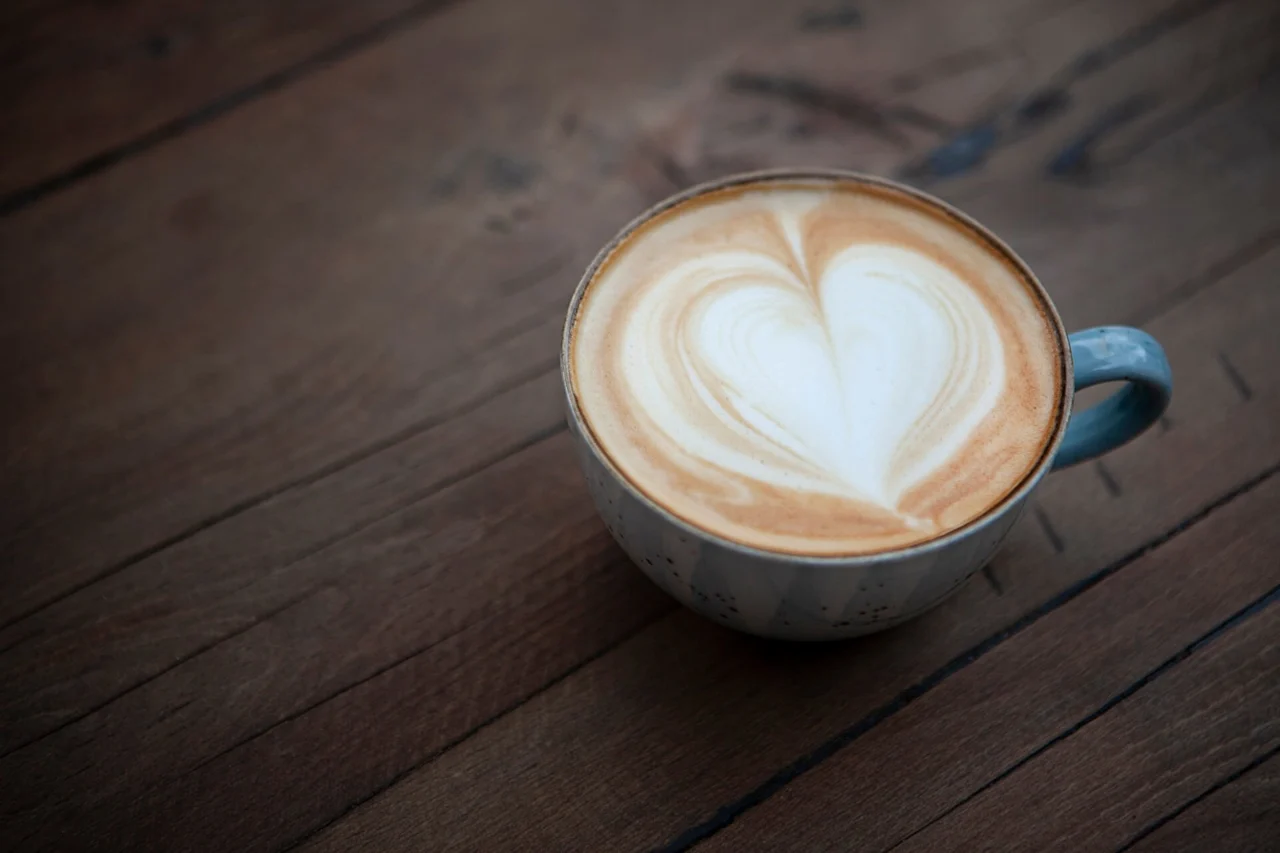 En kopp cappuccino med hjärtformat latteart står på ett träbord och ger en varm, konstnärlig känsla till en mysig miljö.