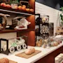 Brødlinper og kurver med frukt står på en trehylle; krukker fylt med frokostblanding og krydder står på en hvit benkeplate. En potteplante tilfører grønt til rommet.