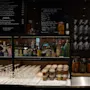 En uppsättning spritflaskor visas bakom en bardisk med staplade glas och burkar med snacks, under en svart menytavla.