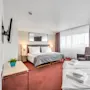 Et hotelværelse med to pænt opredte senge, moderne møbler og store vinduer med både gennemsigtige og ugennemsigtige gardiner.