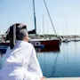 En person i hvit morgenkåpe, med et grått håndkle på hodet, sitter på en brygge og ser utover en marina fylt med seilbåter. Synlig tekst: "ED" på en nærliggende rød båt.