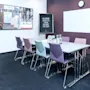 Et konferanserom med et rektangulært bord omgitt av fargerike stoler. På veggen står det "ENJOY YOUR CREATIVE MEETING!" og "CLARION LOVES TO THINK OUTSIDE THE BOX!" En klokke og et skap er til stede.