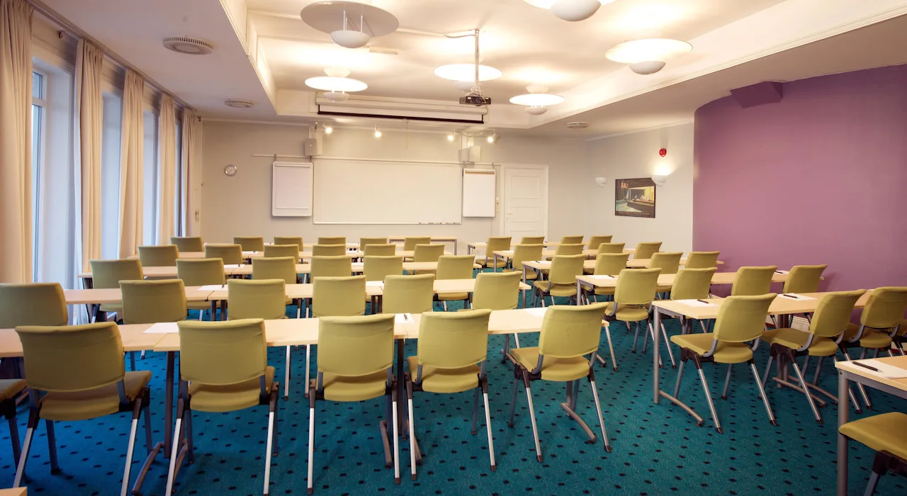 Rows of green chairs facing a whiteboard in an empty conference room with purple walls.