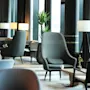 Luxurious lounge chairs sit quietly in a modern hotel lobby, surrounded by contemporary decor, potted plants, and soft lighting, creating an inviting and serene atmosphere.