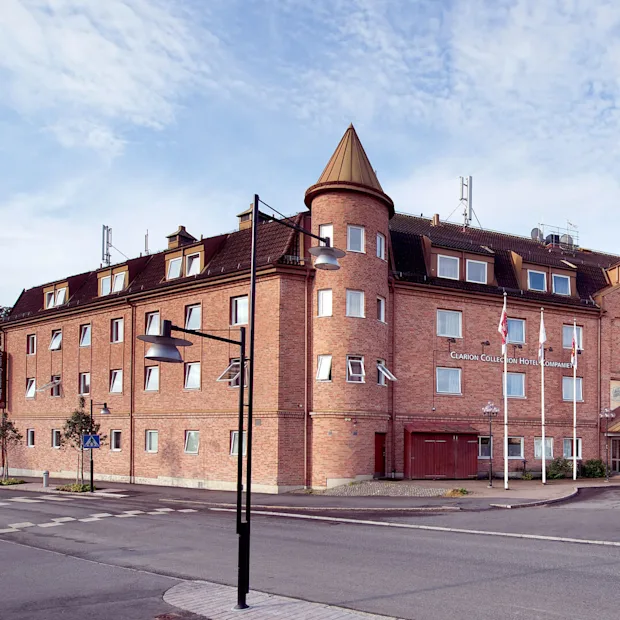 En tegelsten byggnad med koniska torn står vid ett gatuhörn under en delvis molnig himmel.