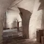 En rustikk vinkjeller med steinvegger og hvelvet tak. Et trebord har en vinflaske og glass, omgitt av dempet belysning. Trelåder hviler i nærheten.