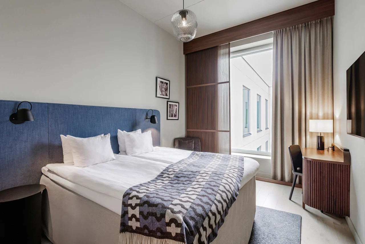 En snyggt ordnat hotellrum med dubbelsäng, mjukt ljus och modern inredning som utstrålar komfort och enkelhet.